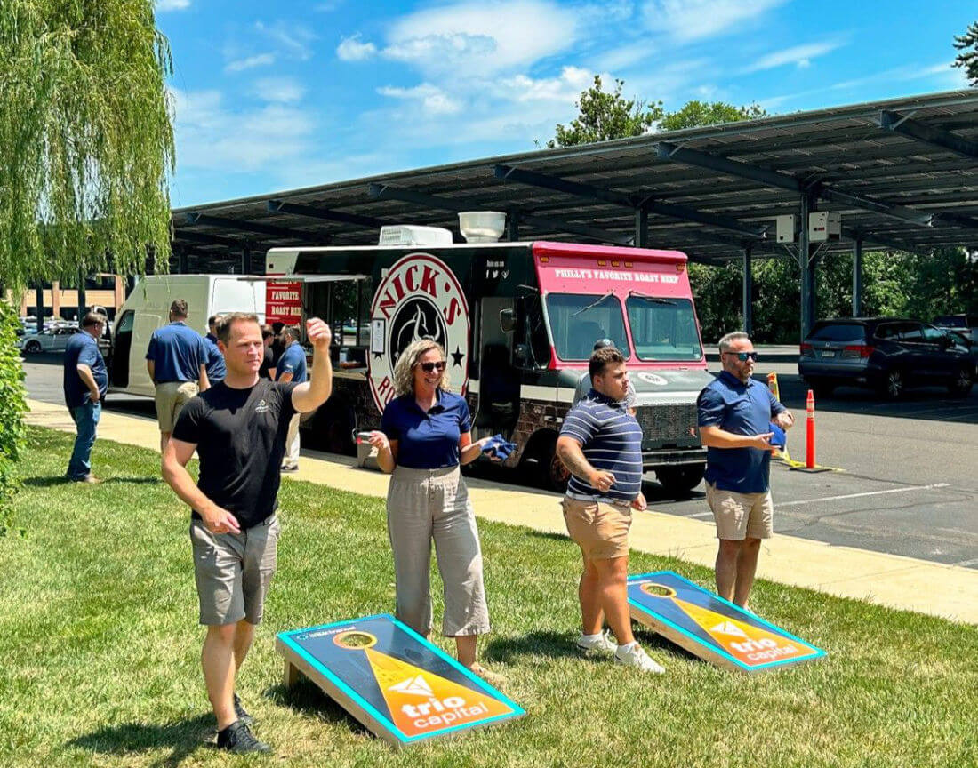 Four people playing corn hole outside, in front of a food truck.