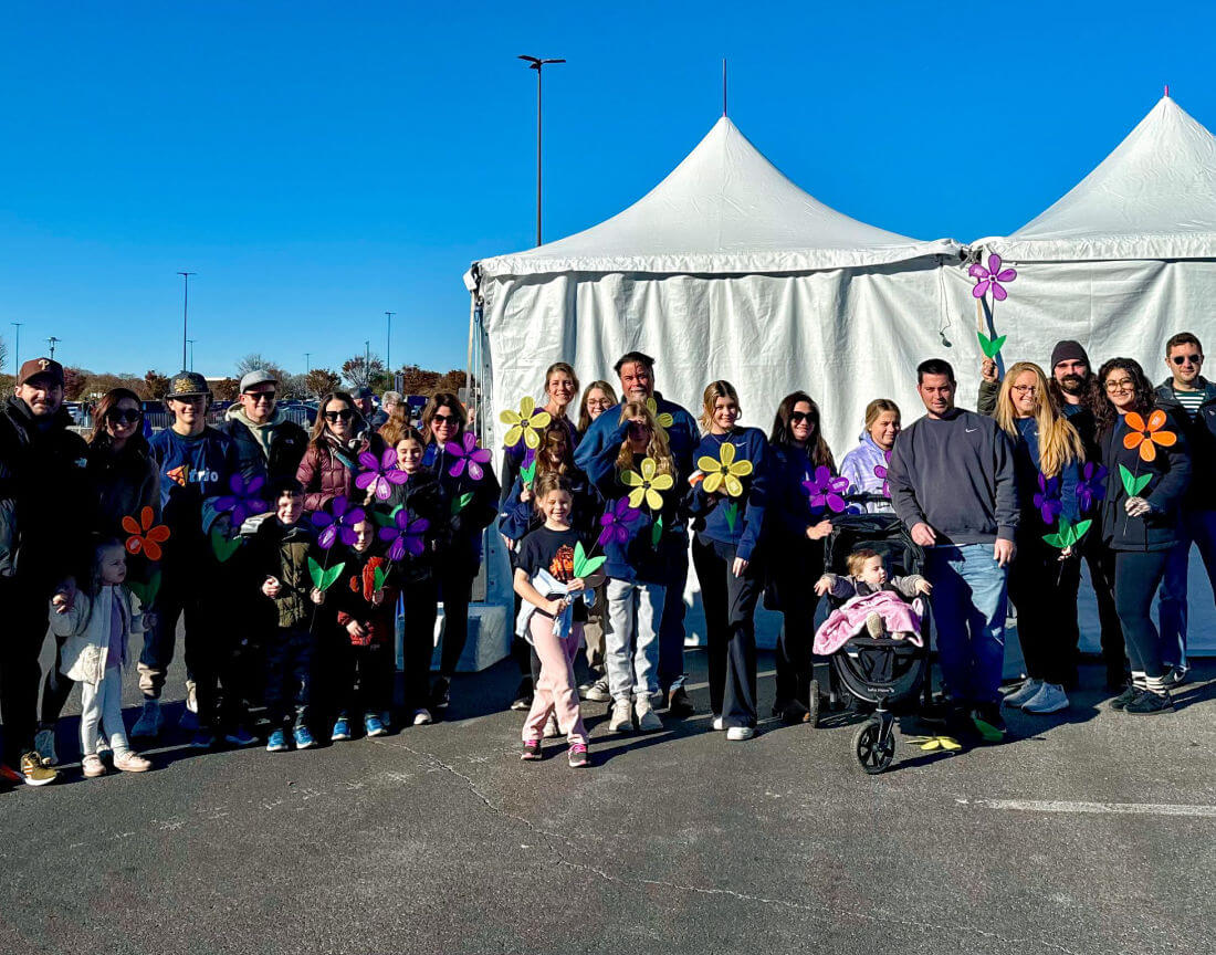 A group of people outside, in front of white tents, holding plastic flowers